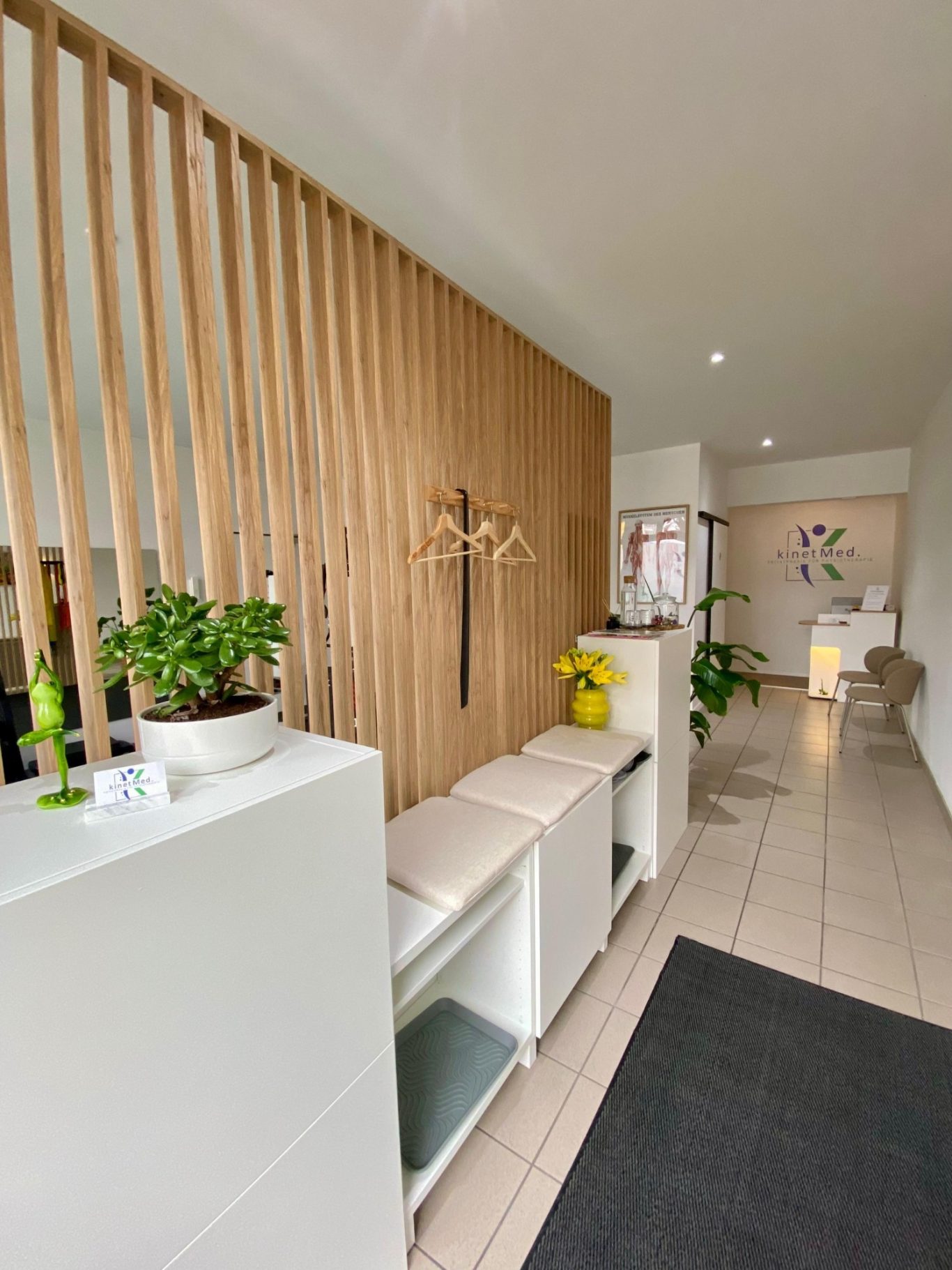 Moderner Empfangsbereich der Physiotherapie kinetMed München mit Holz und weißen Möbeln.