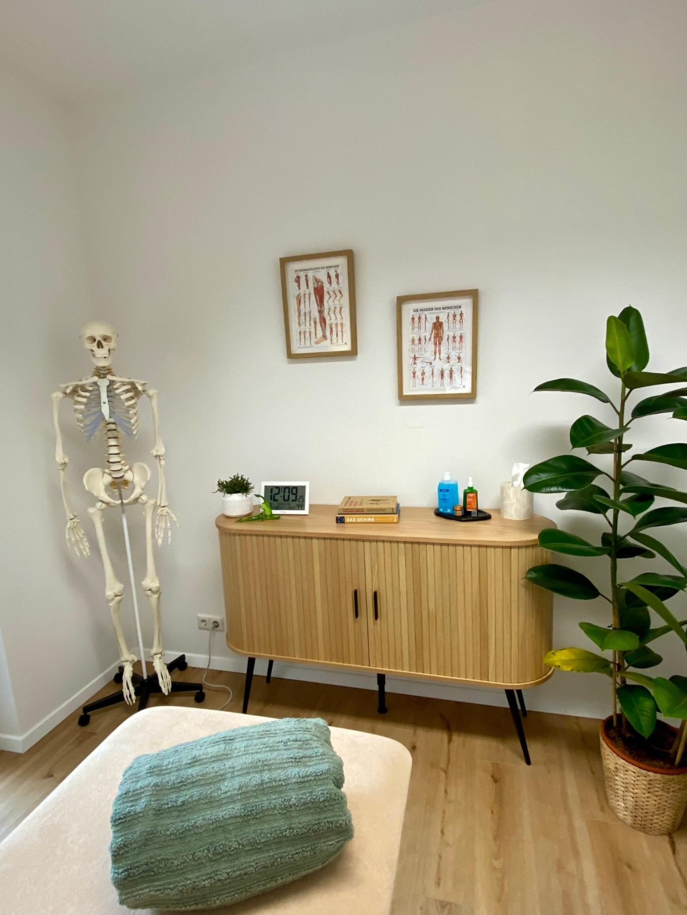 Moderner Behandlungsraum der Physiotherapie kinetMed München mit Skelettmodell, Holzkommode und freundlicher Atmosphäre.