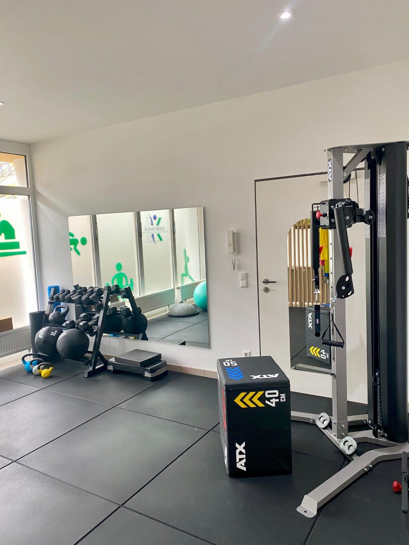 Heller Trainingsraum der Physiotherapie kinetMed München Sendling mit Seilzug, Plyo Box und großem Spiegel.